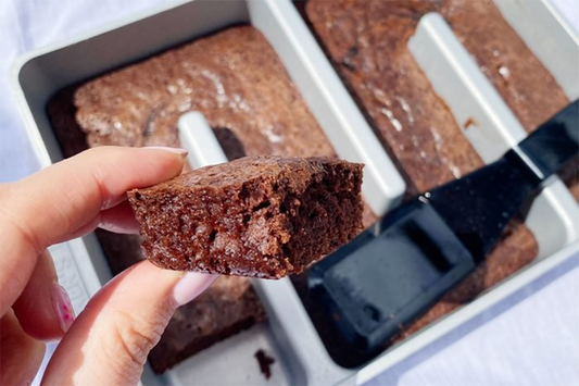 Baker's Edge brownie edge pan shown with brownies in it, and a hand holding up a delicious slide of chocolate brownie.